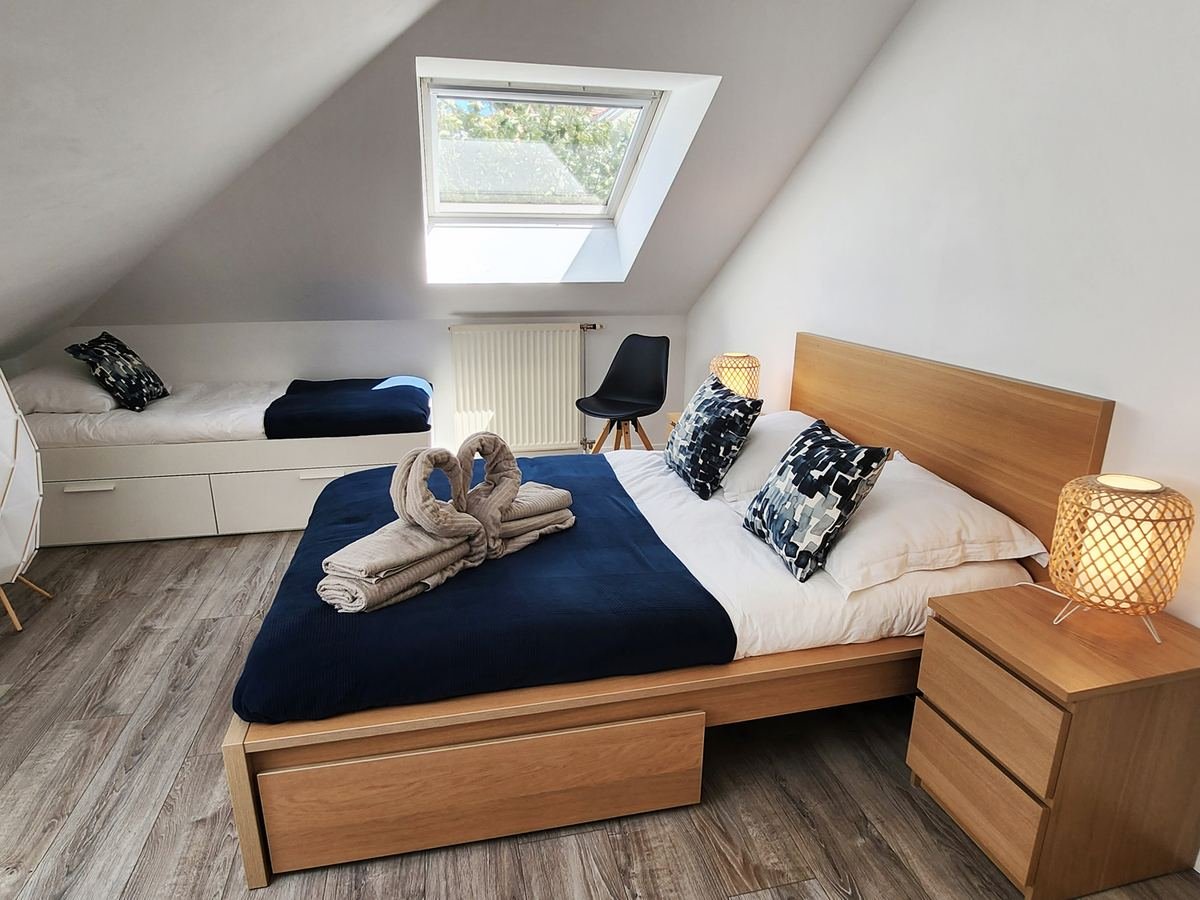 Chambre mansardée d’Akela avec lit double, lit simple d’appoint et bureau sous la fenêtre de toit